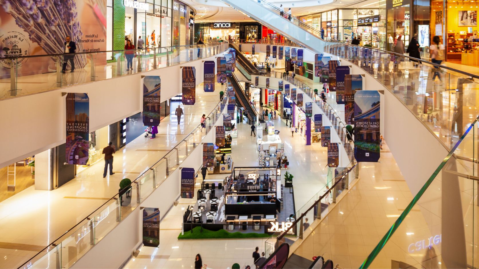 Vista panorámica del interior de un centro comercial moderno con varios niveles, tiendas, pasillos y visitantes.